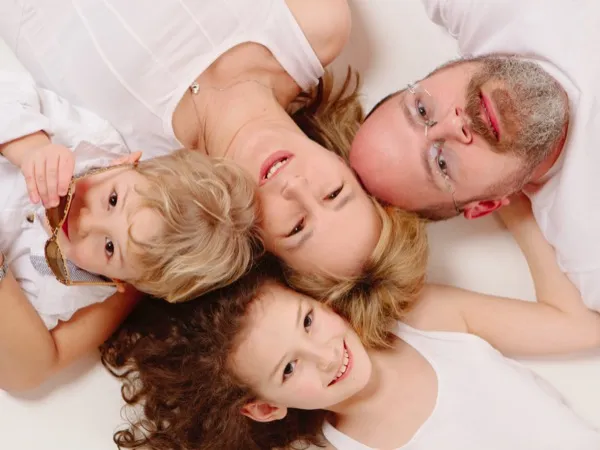 Familie liegt auf weißem Boden, Köpfe eng zusammen, Blick von oben